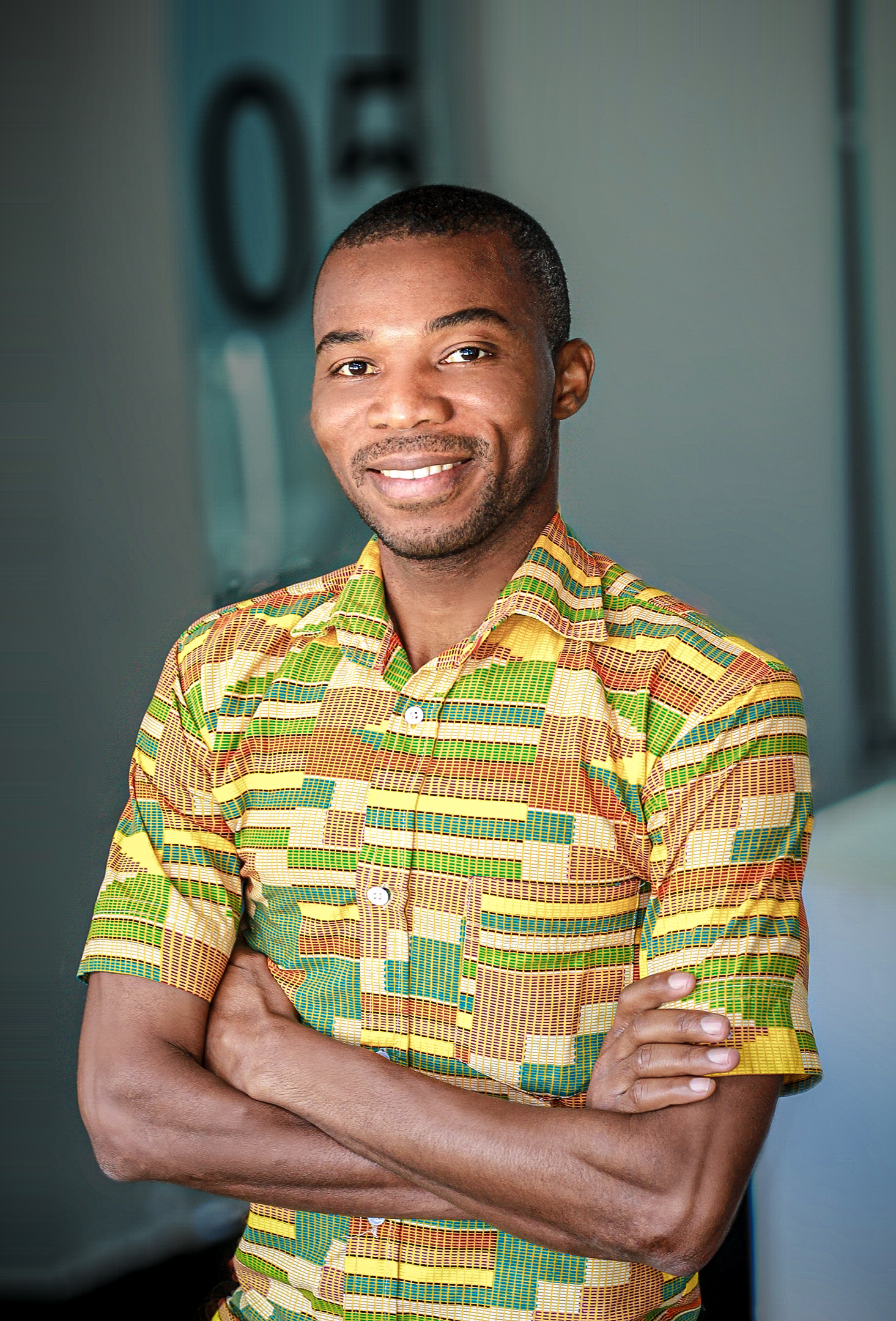 Senakpon Fabrice Fidèle Kpoholo, educador beninense, sorrindo de braços cruzados com camisa de tecido africano